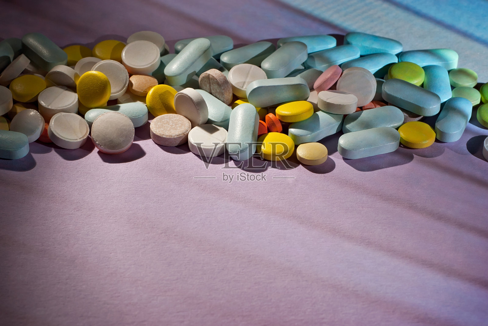 白色，黄色，红色，橙色和蓝色药丸在紫色纸板背景。用药在一个黑暗的背景与对比戏剧性的光。照片摄影图片