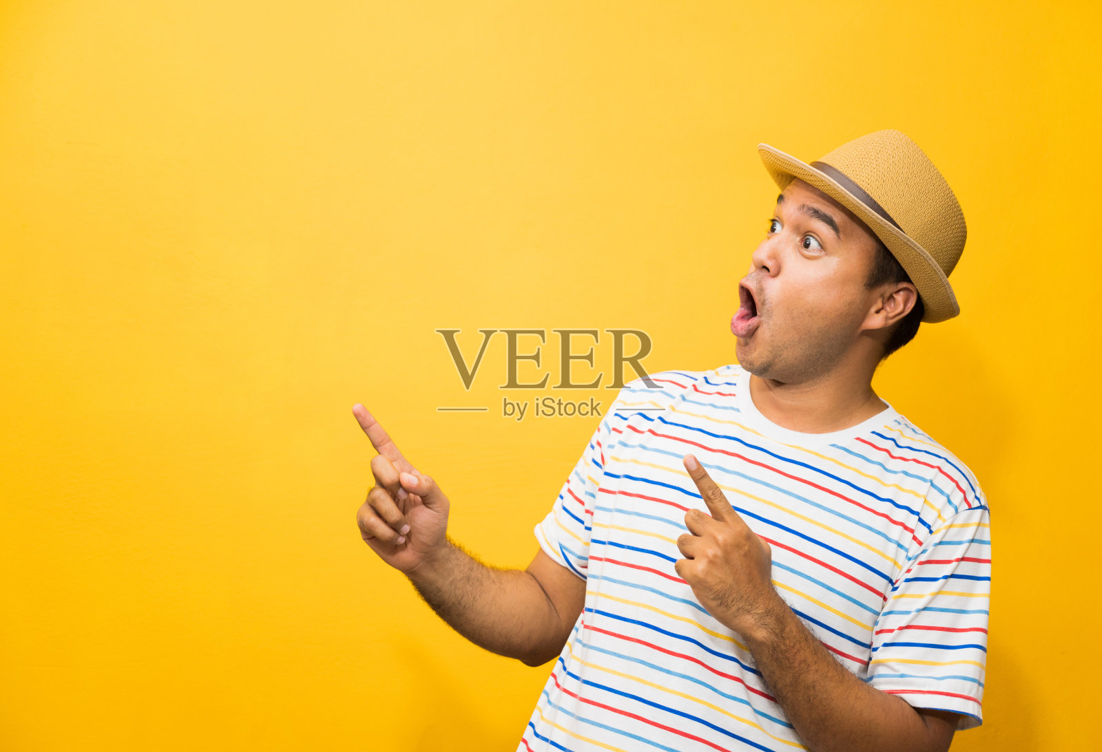 年轻的快乐和有趣的亚洲人指着手指空白的文字在黄色的背景。照片摄影图片