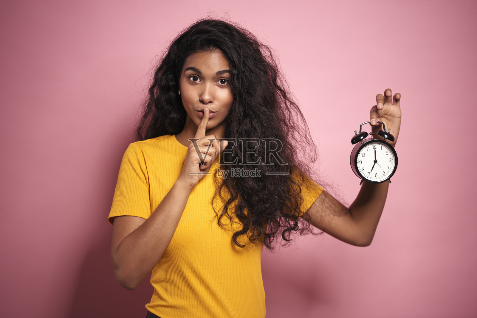 非洲妇女手指放在嘴唇上，拿着闹钟。照片摄影图片