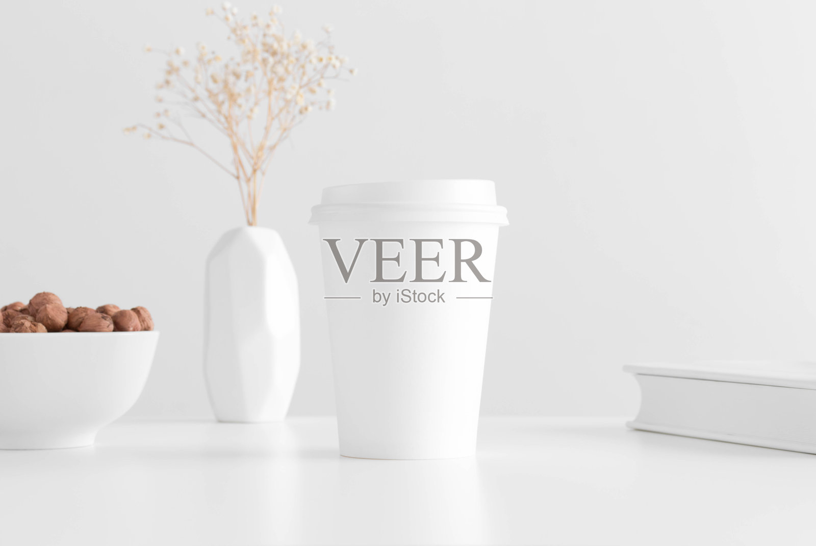 咖啡纸杯模型花瓶里有一只吉普赛菲拉，白色桌子上放着榛子和一本书照片摄影图片