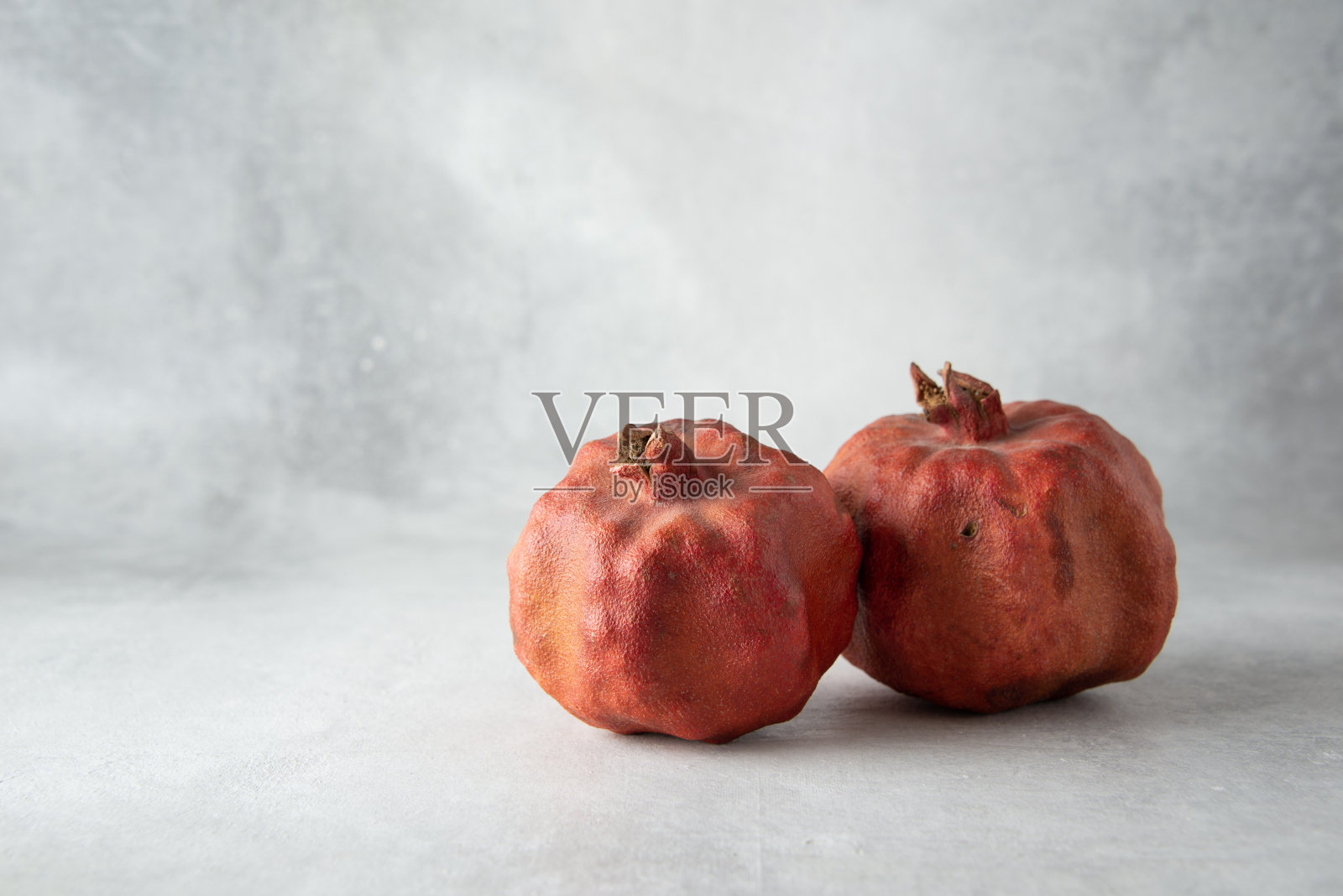 两个干燥丑陋的石榴在灰色的背景与复制空间。照片摄影图片