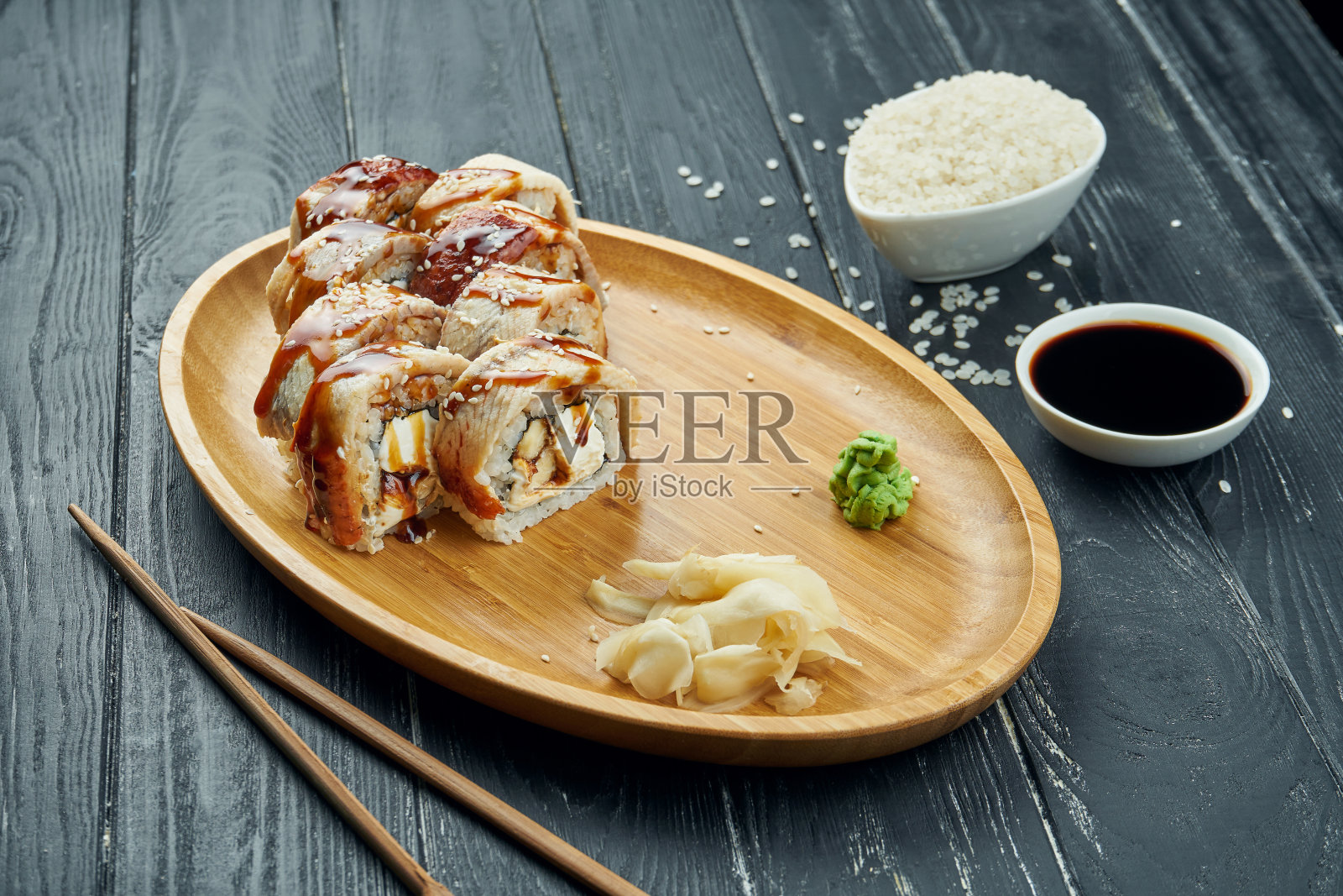 经典的日本寿司卷——卷上奶油芝士、鳗鱼和鳗鱼酱，放在竹制的盘子里，背景是黑色的木头照片摄影图片