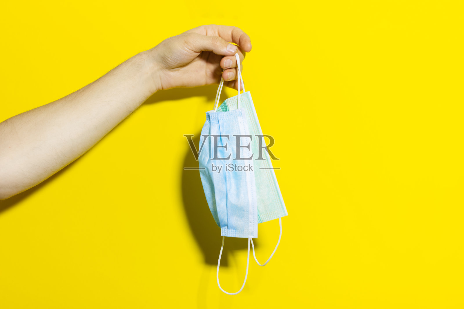 工作室的特写，男性手拿两个医疗流感口罩对抗冠状病毒隔离在黄色背景。照片摄影图片