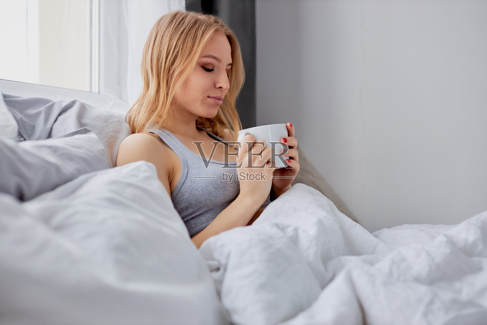 甜美的女孩躺在床上，喝着一杯热咖啡照片摄影图片