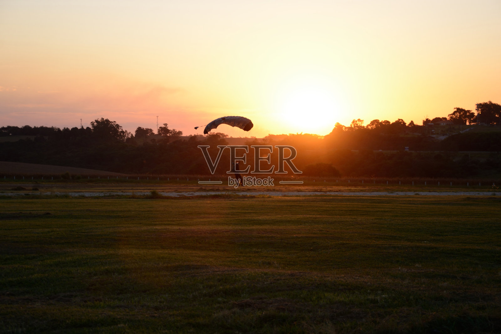 跳伞者和日落在绿色的田野照片摄影图片