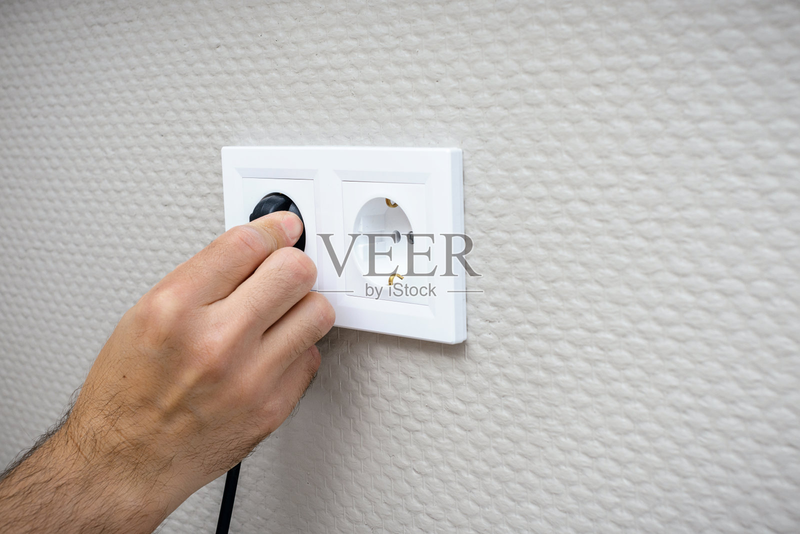 插电，黑色插头插在墙上白色插座上。照片摄影图片