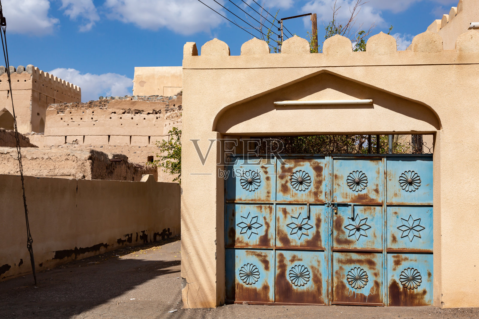 阿曼Al Mudairib古镇墙壁上带有装饰的蓝色锈迹大门照片摄影图片