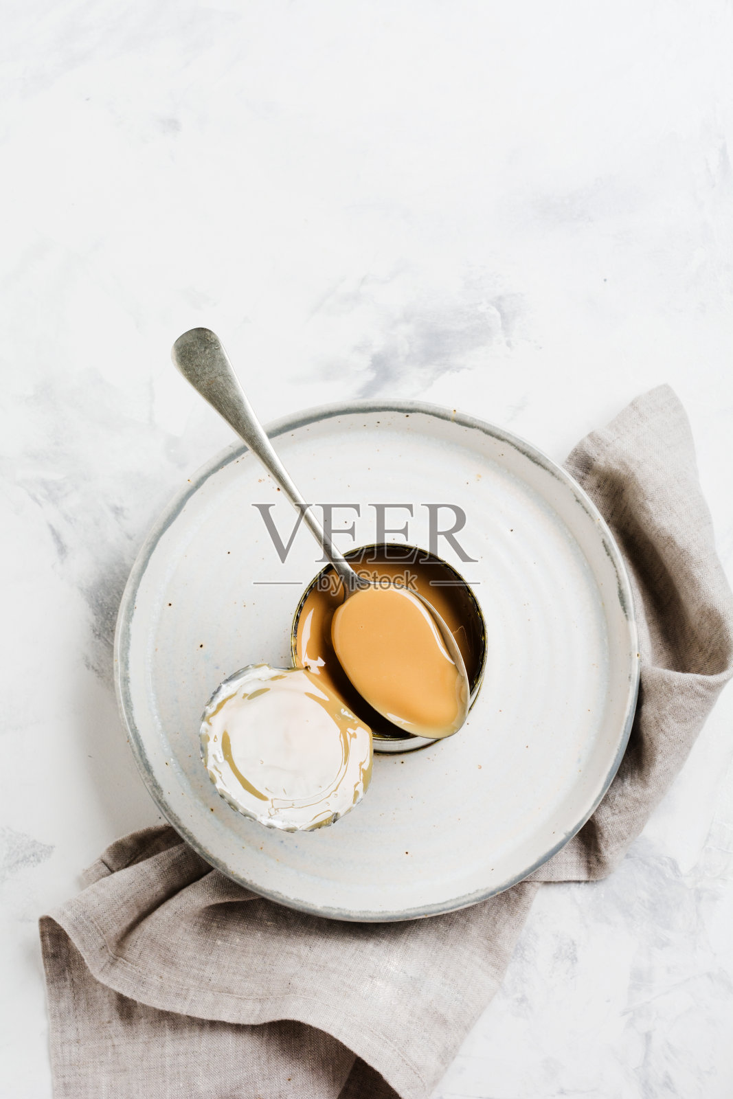 炼乳或淡炼乳放在敞口的罐子里，放在轻质混凝土桌上。前视图。照片摄影图片