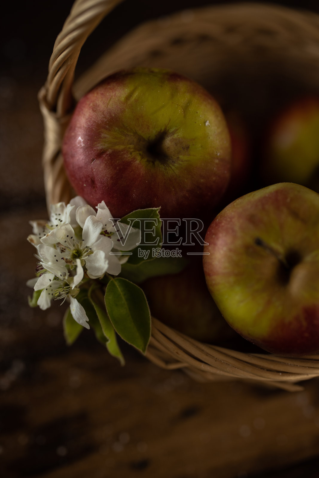 鲜红的苹果和花枝放在篮子里，背景是深色的木头照片摄影图片