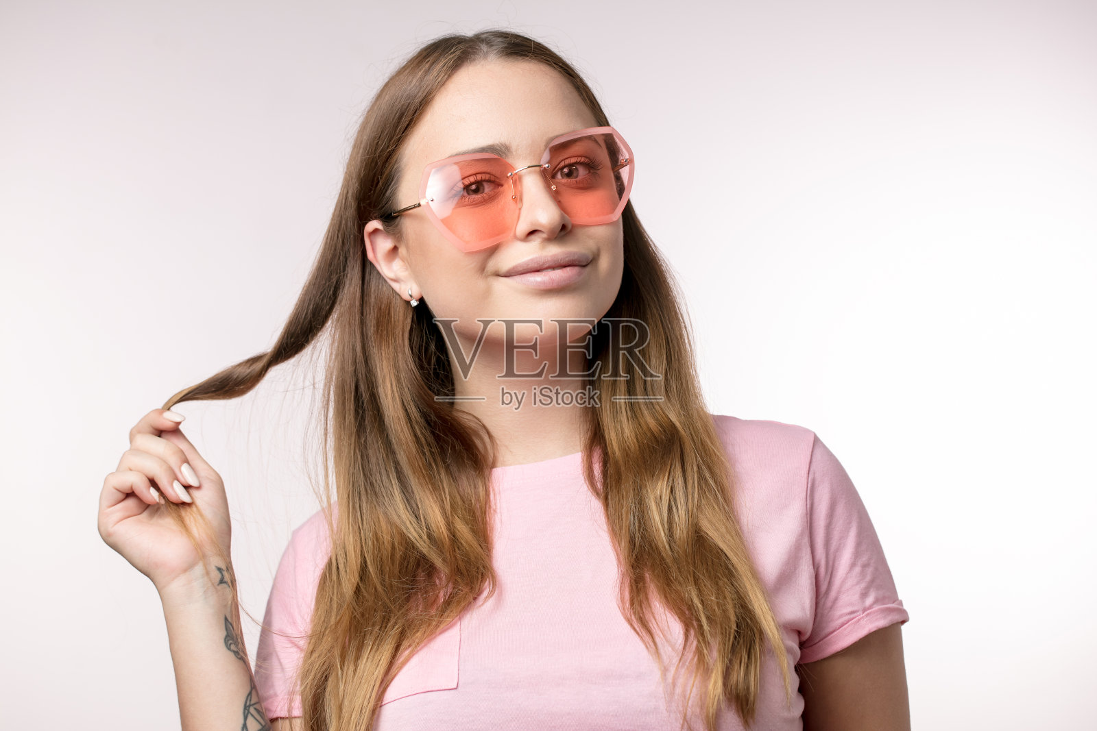 微笑着的了不起的女人摸着她的头发摆着粉色的姿势，有趣的太阳镜照片摄影图片