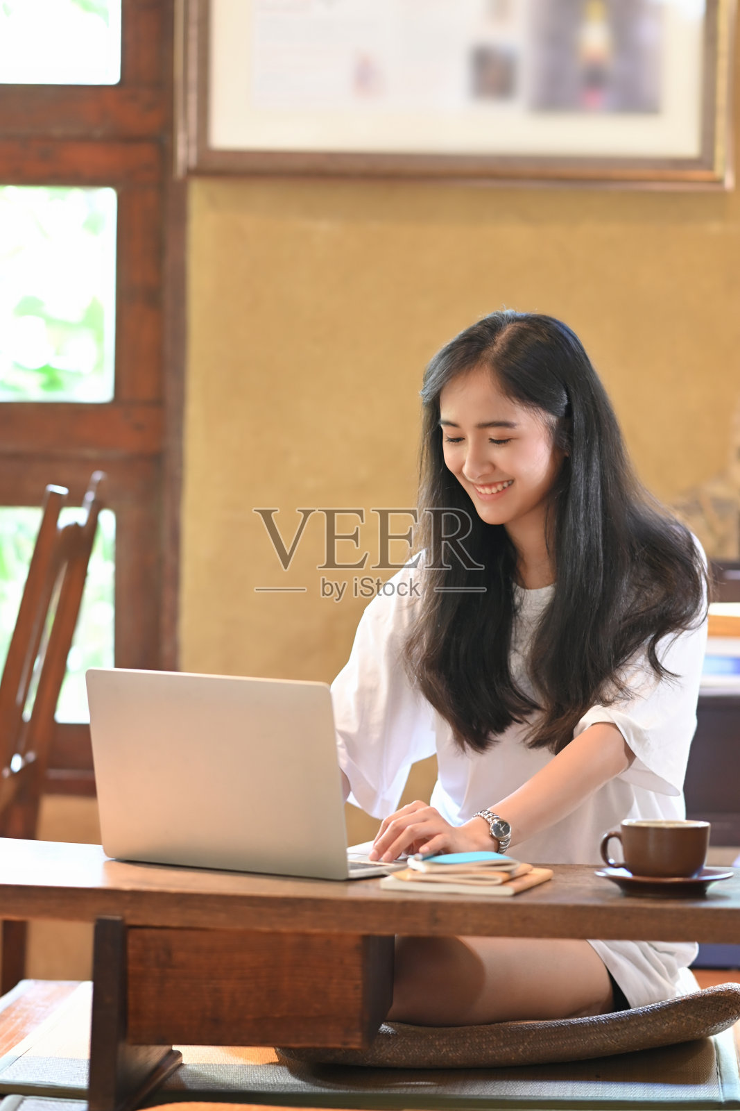 迷人的亚洲女人的照片与电脑笔记本电脑，把周围的咖啡杯和笔记本堆在复古客厅作为背景木制办公桌。照片摄影图片