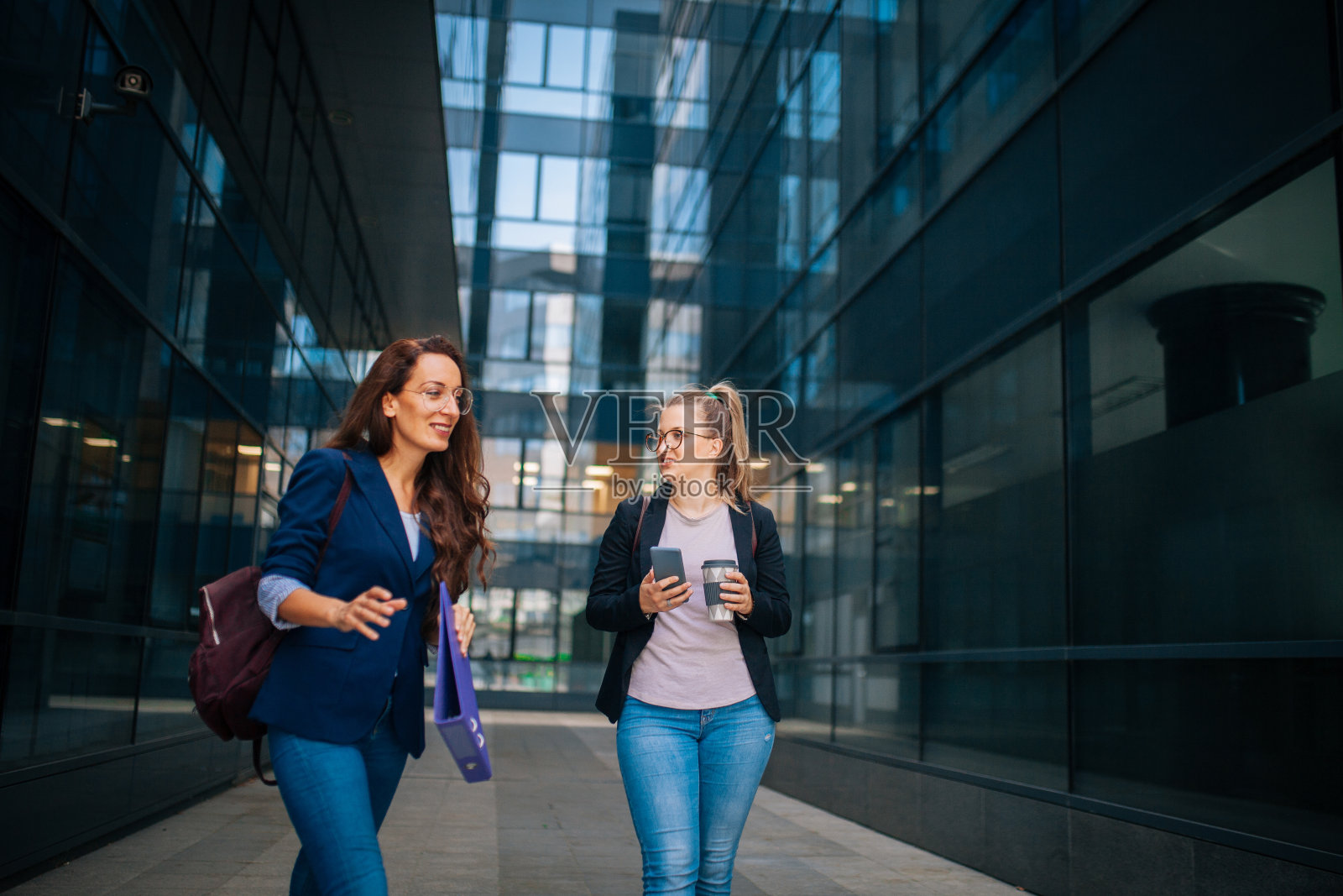 年轻漂亮的女商人在室外谈话。办公楼背景。照片摄影图片