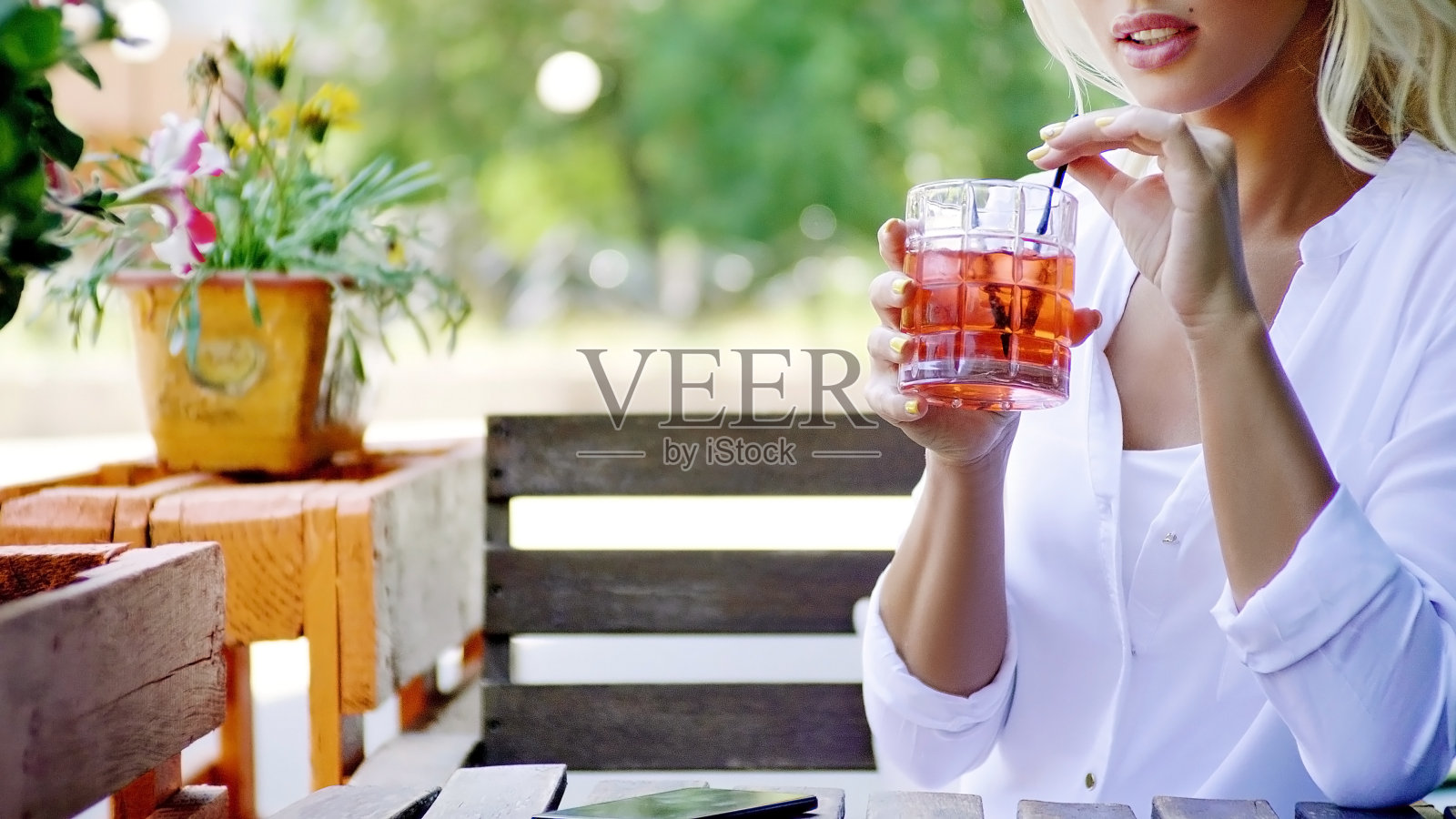 一个迷人的年轻金发女人在白衬衫喝鸡尾酒的近距离，坐在现代餐厅的阳台上在一个阳光明媚的夏天。照片摄影图片