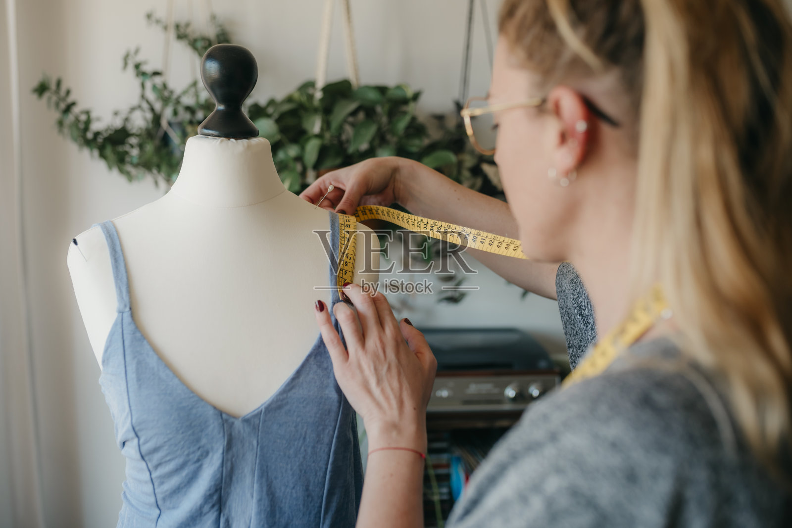 年轻女性时装设计师测量人体模型，女裁缝拿着胶带与假人在舒适的家或裁缝店工作，服装制作和缝纫概念，照片摄影图片