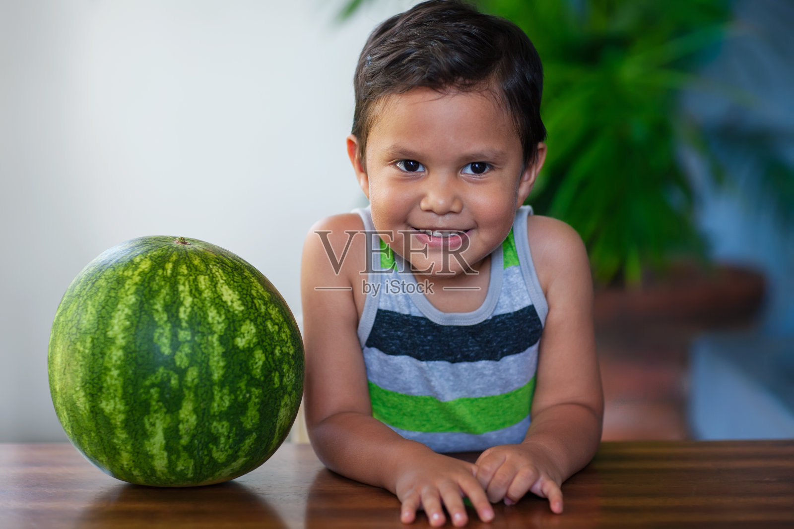 一个可爱的小男孩坐在一个成熟的西瓜旁边，他将吃作为低卡路里和营养的款待。照片摄影图片