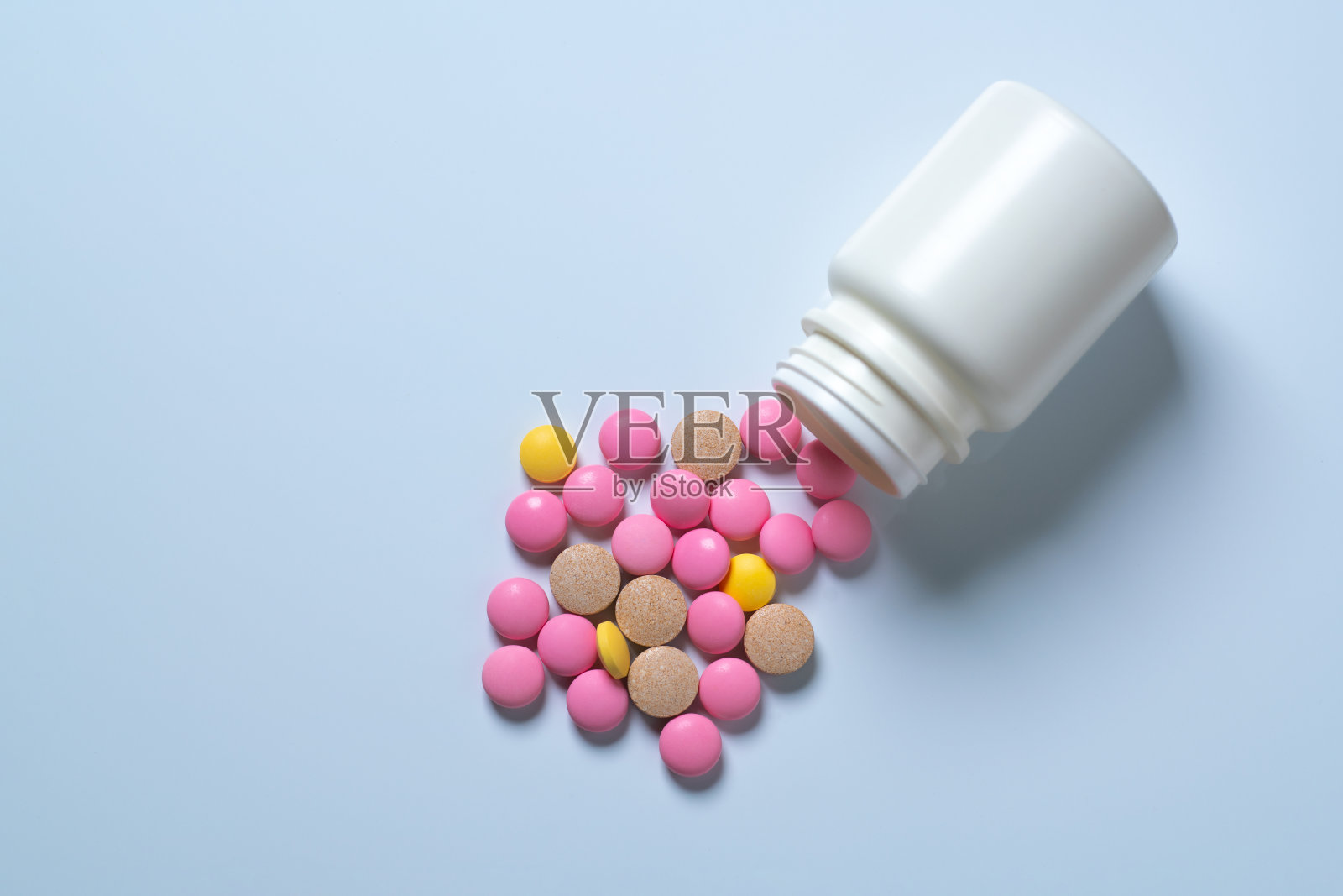 白色背景下的一个白色罐子里溢出了五颜六色的药丸照片摄影图片