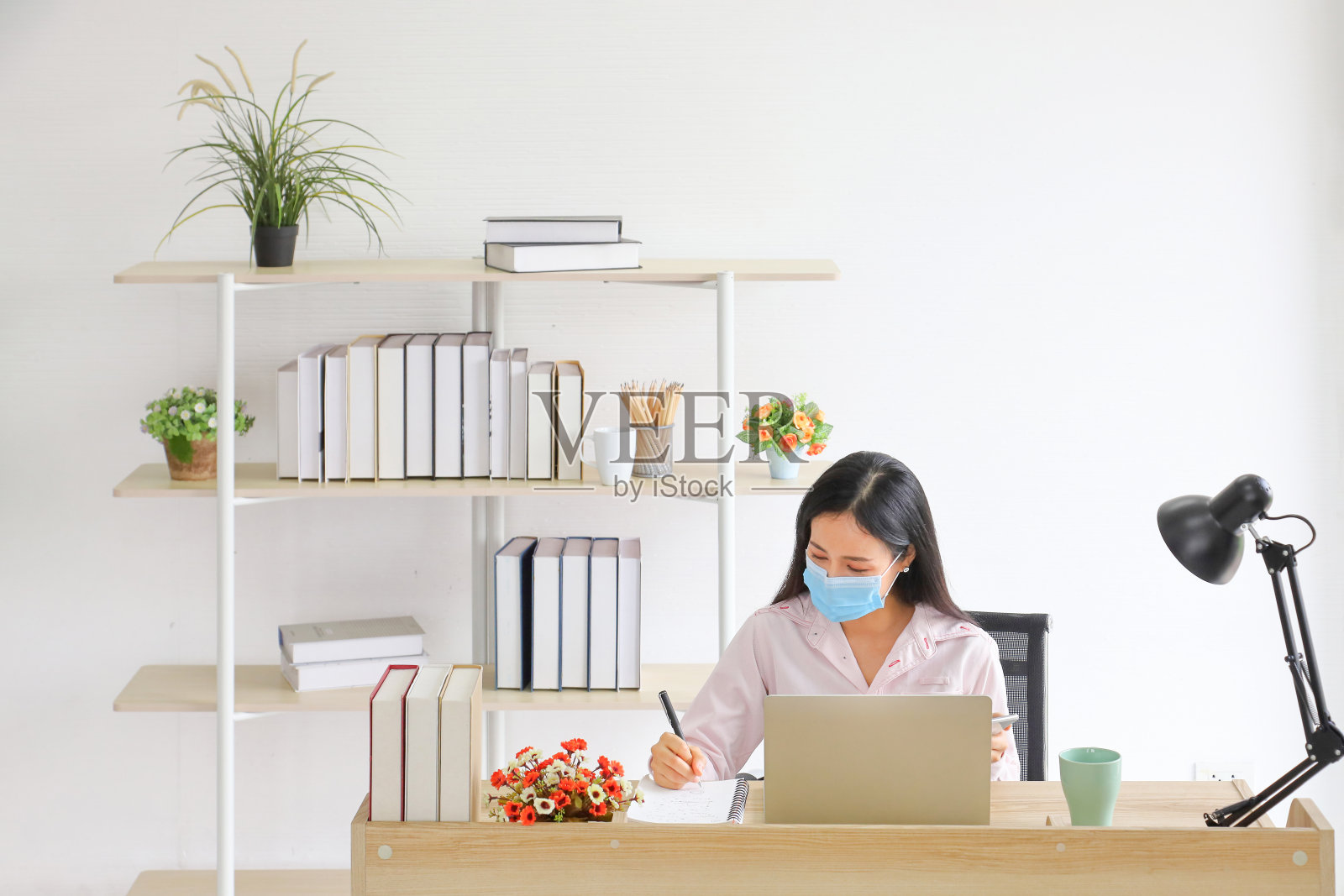 在新冠病毒或新冠病毒疫情发生后的新常态变化期间，作为业务办公室的社交距离政策，佩戴医用口罩在家工作的女性员工照片摄影图片