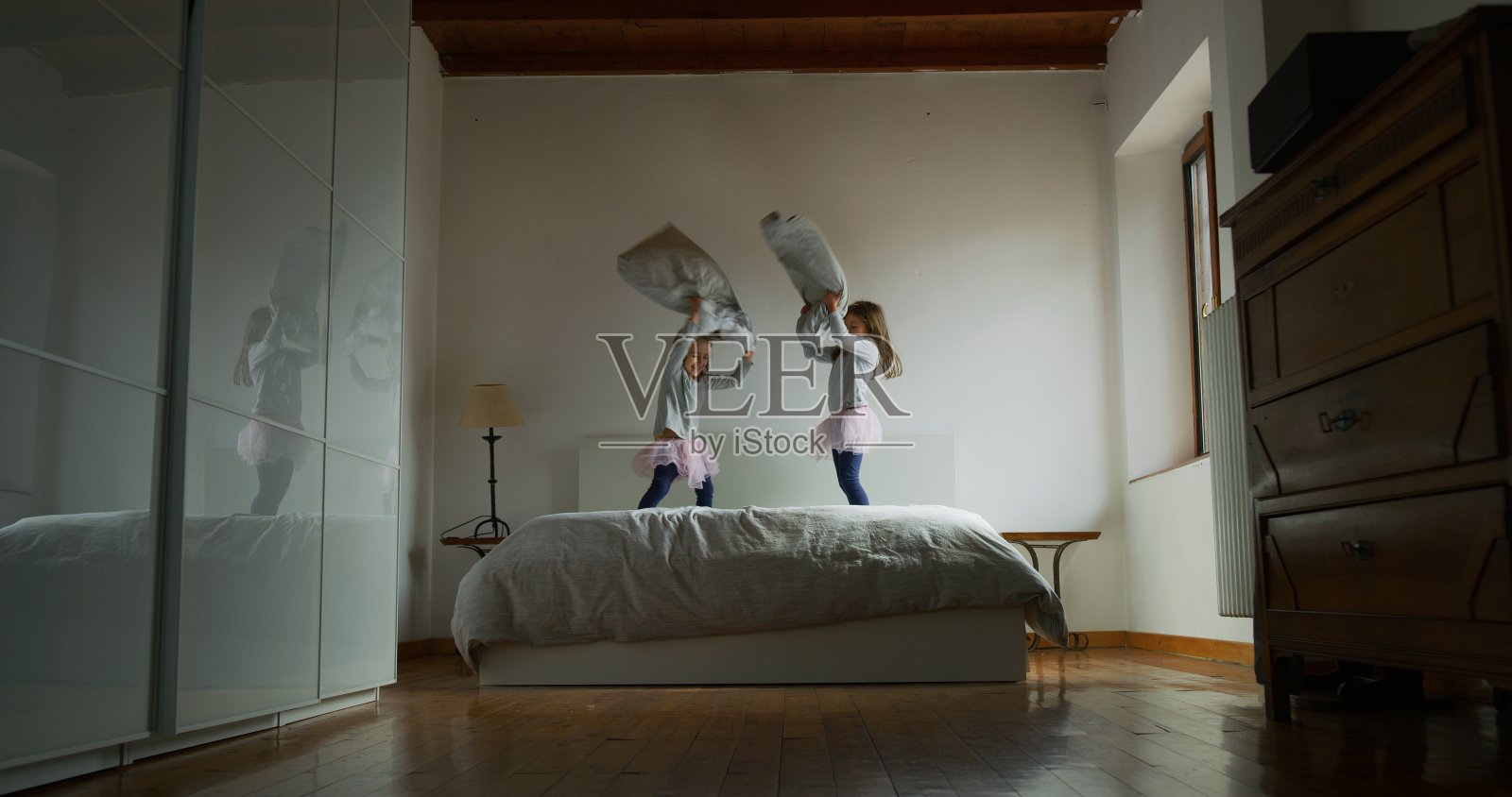 两个小女孩在他们父母的床上蹦蹦跳跳的肖像照片摄影图片