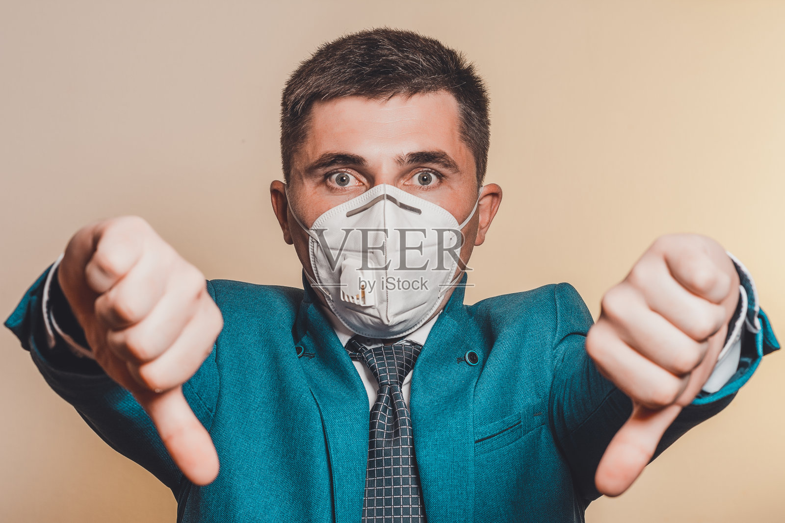 坚强的男人、打着领带、戴着医用口罩的商人，展示了在新冠肺炎疫情中工作的信心。用大拇指表示经济危机期间的不满和沮丧。照片摄影图片