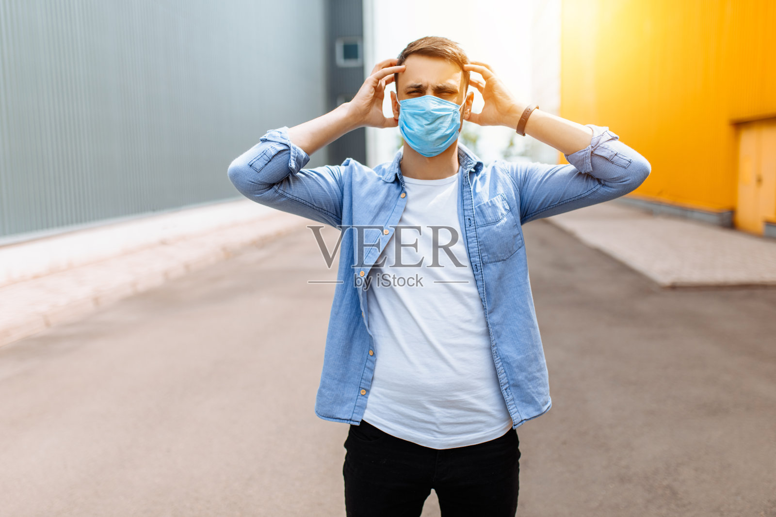 一名惊慌失措的男子戴着医用防护面具，恐惧地抬起头，站在城市的露天里照片摄影图片