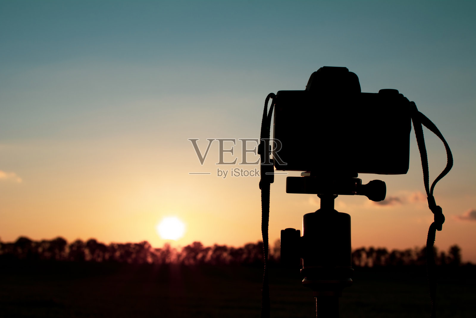 三脚架上的一台照相机的剪影，在草坪上拍摄红色的日落照片摄影图片