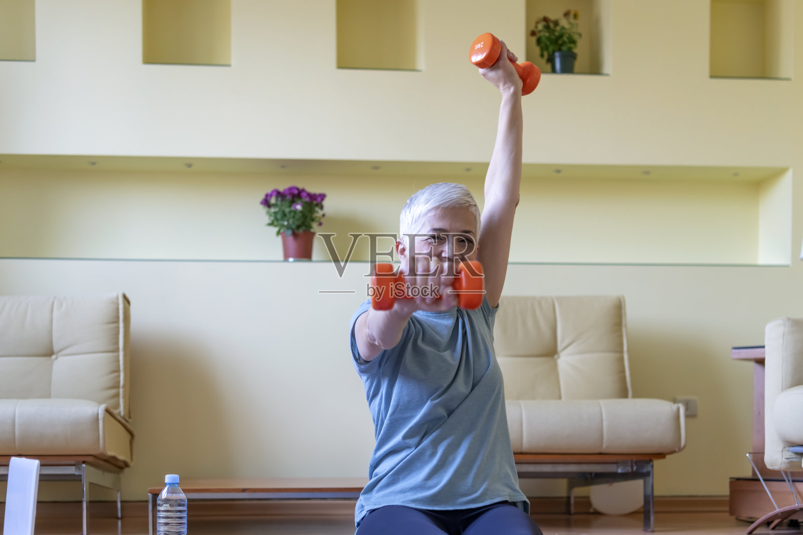 成熟女性在家锻炼。老年妇女举哑铃的肖像。快乐的老女人用哑铃做健身训练-隔离照片摄影图片
