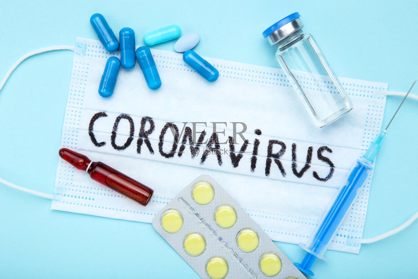 文字冠状病毒与药丸，注射器和安瓿在蓝色背景照片摄影图片