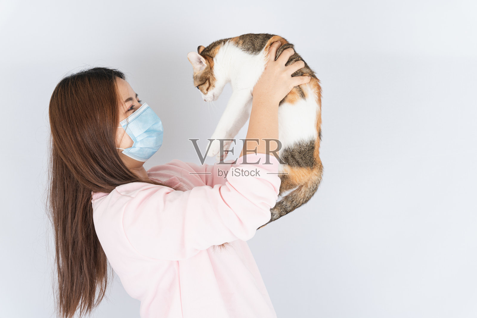 亚洲美丽快乐的女人戴着医用防护口罩，保护冠状病毒，过滤粉尘PM 2.5，对猫毛感冒和过敏，她带着一只猫在白色的背景照片摄影图片