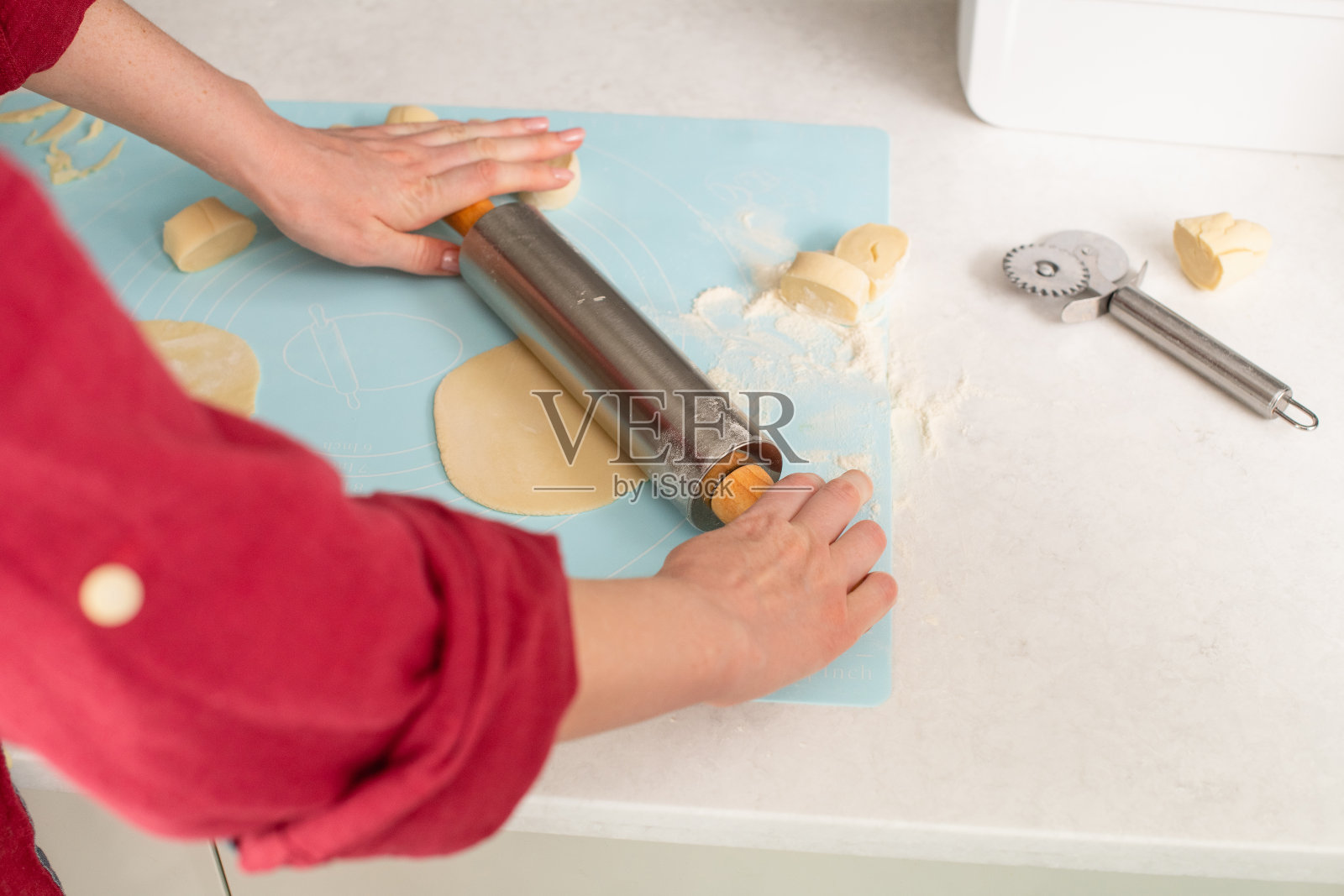 女性手用现代金属和木制大头针和硅胶蓝垫烹饪糕点，面团切割机在桌子上，家庭主妇在室内根据食谱烘焙饼干照片摄影图片