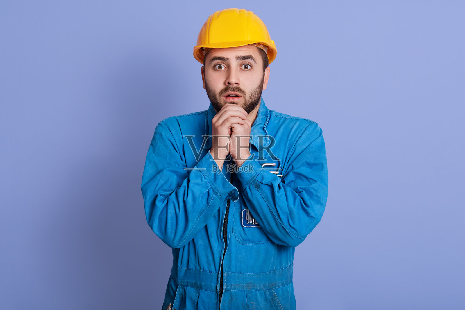 这是一幅惊恐的年轻建筑工人的肖像，他睁大了眼睛，直视着镜头，双手合十，因为害怕冠状病毒带来的危机。工作问题的概念。照片摄影图片