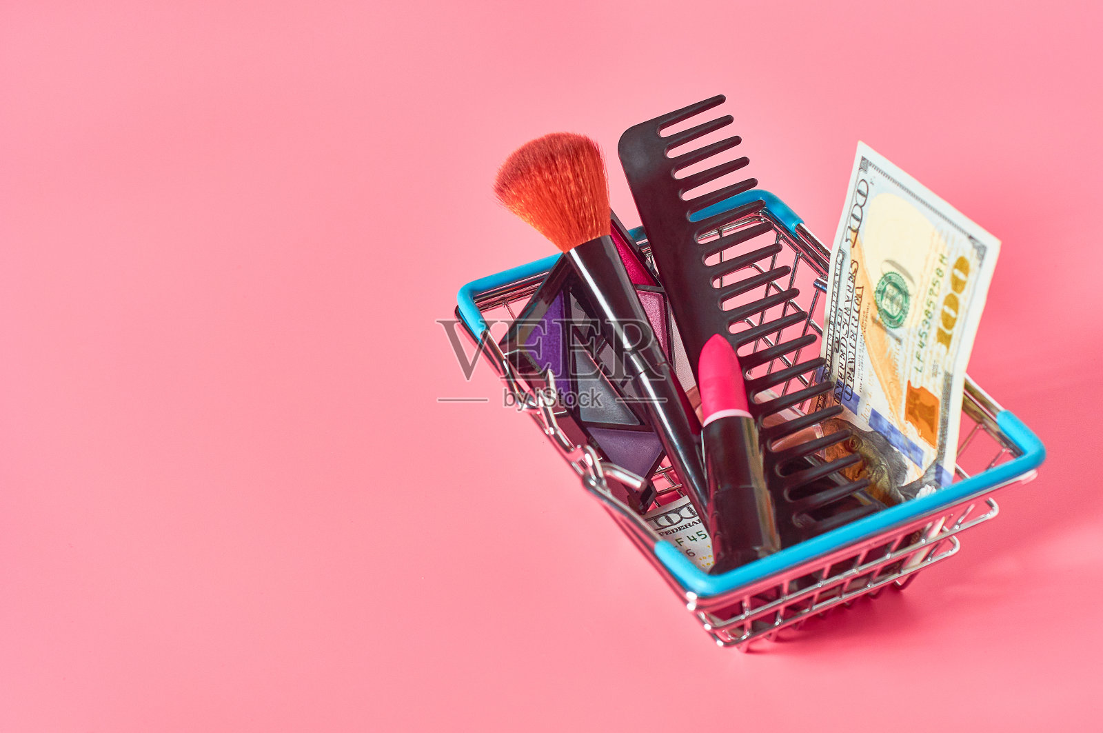 各种化妆品配件和百元钞票在市场篮子粉红色的背景。经营理念照片摄影图片