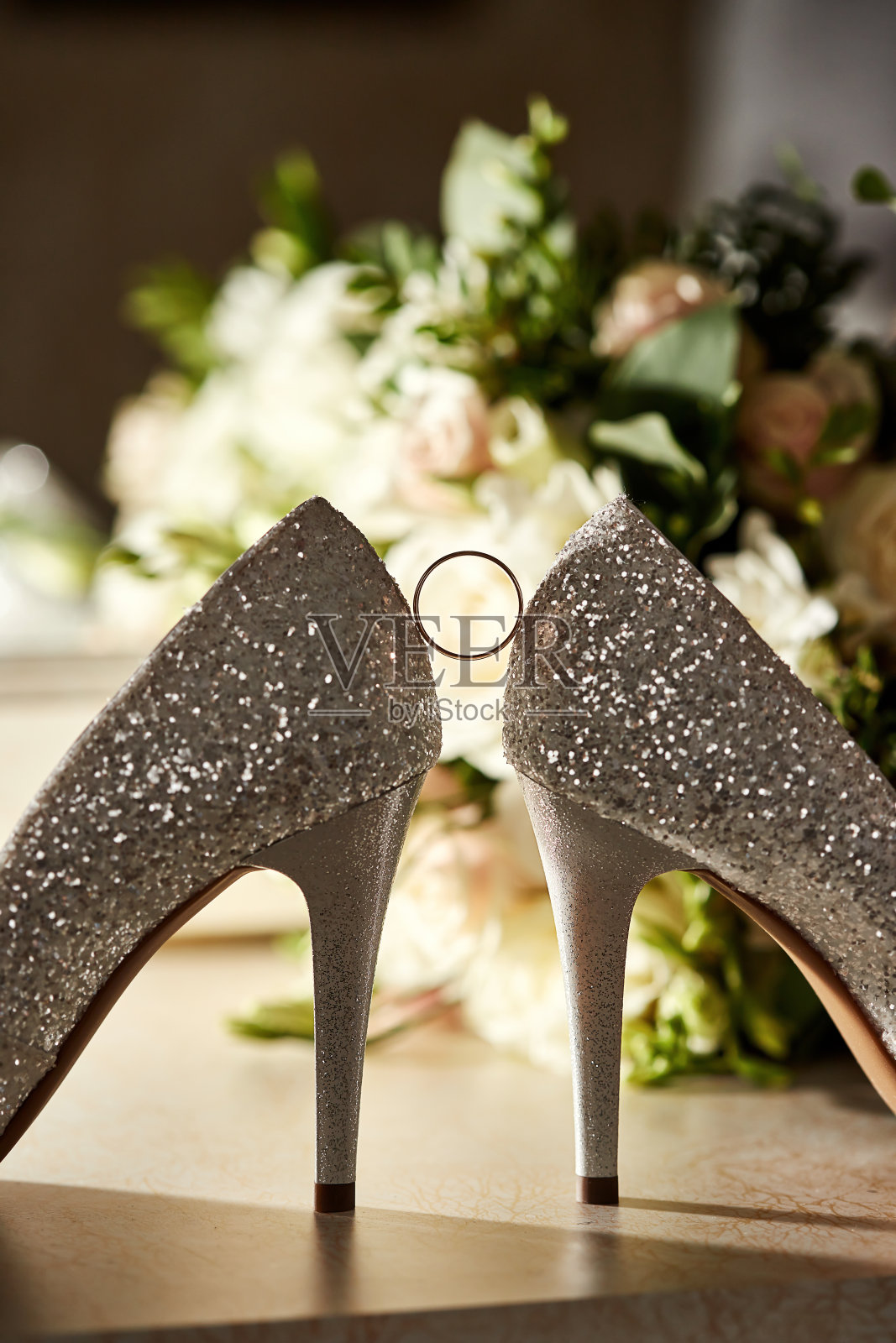 新娘的鞋子之间放着婚戒，背景中还洒着香水照片摄影图片