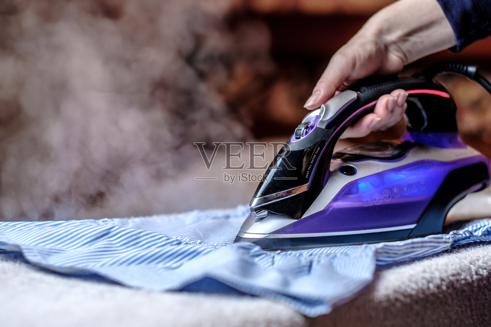特写女性的手在桌子上熨衣服。一阵阵热气腾腾。照片摄影图片