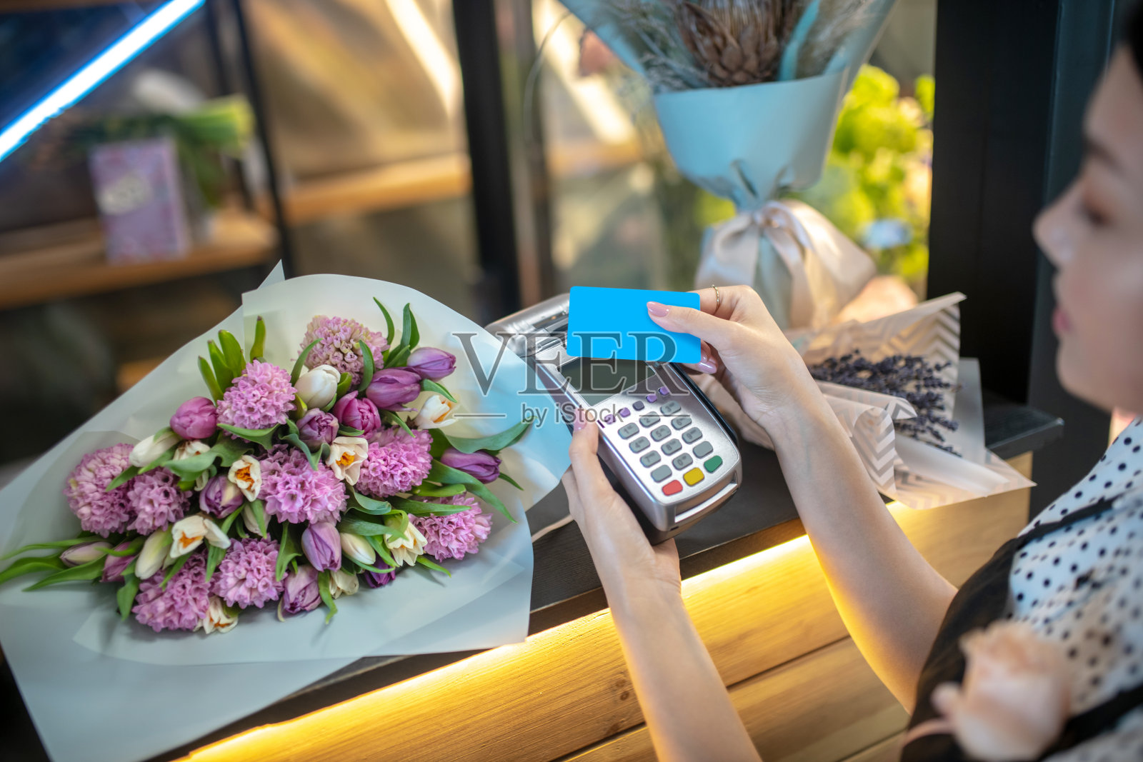 穿着围裙的黑发女性，拿着卡靠近支付终端照片摄影图片