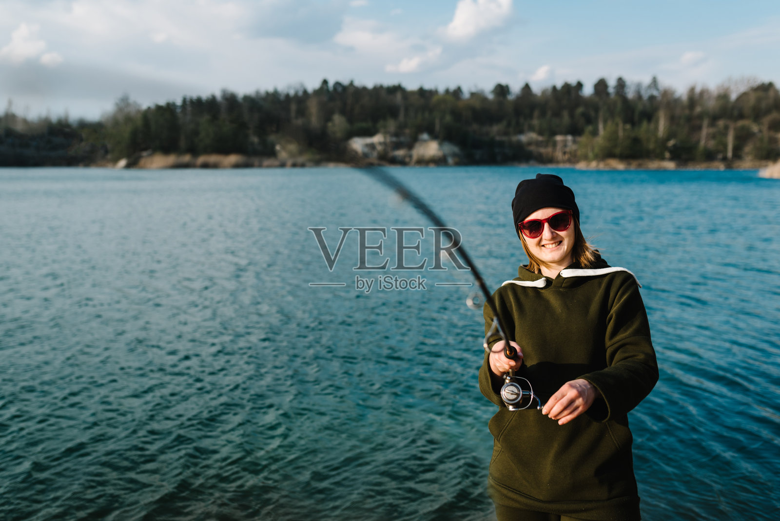 渔夫拿着钓竿，在河岸上旋转卷轴。日出。捕狗鱼、鲈鱼、鲤鱼。乡村度假的概念。女人抓鱼，拉杆而从湖或池塘钓鱼与文本空间。照片摄影图片