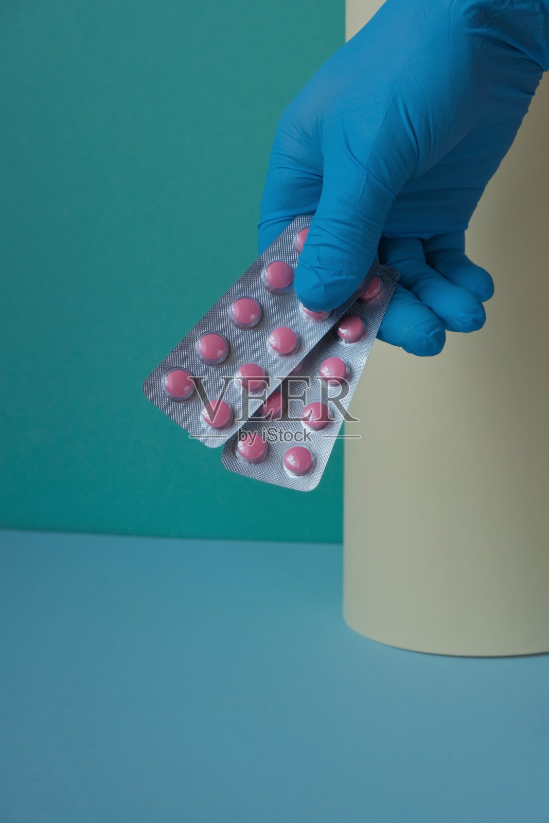 健康医学理念。用药物治疗。手里拿着粉色药丸，戴着蓝色手套，背景是黄绿色。病毒性疾病的治疗照片摄影图片