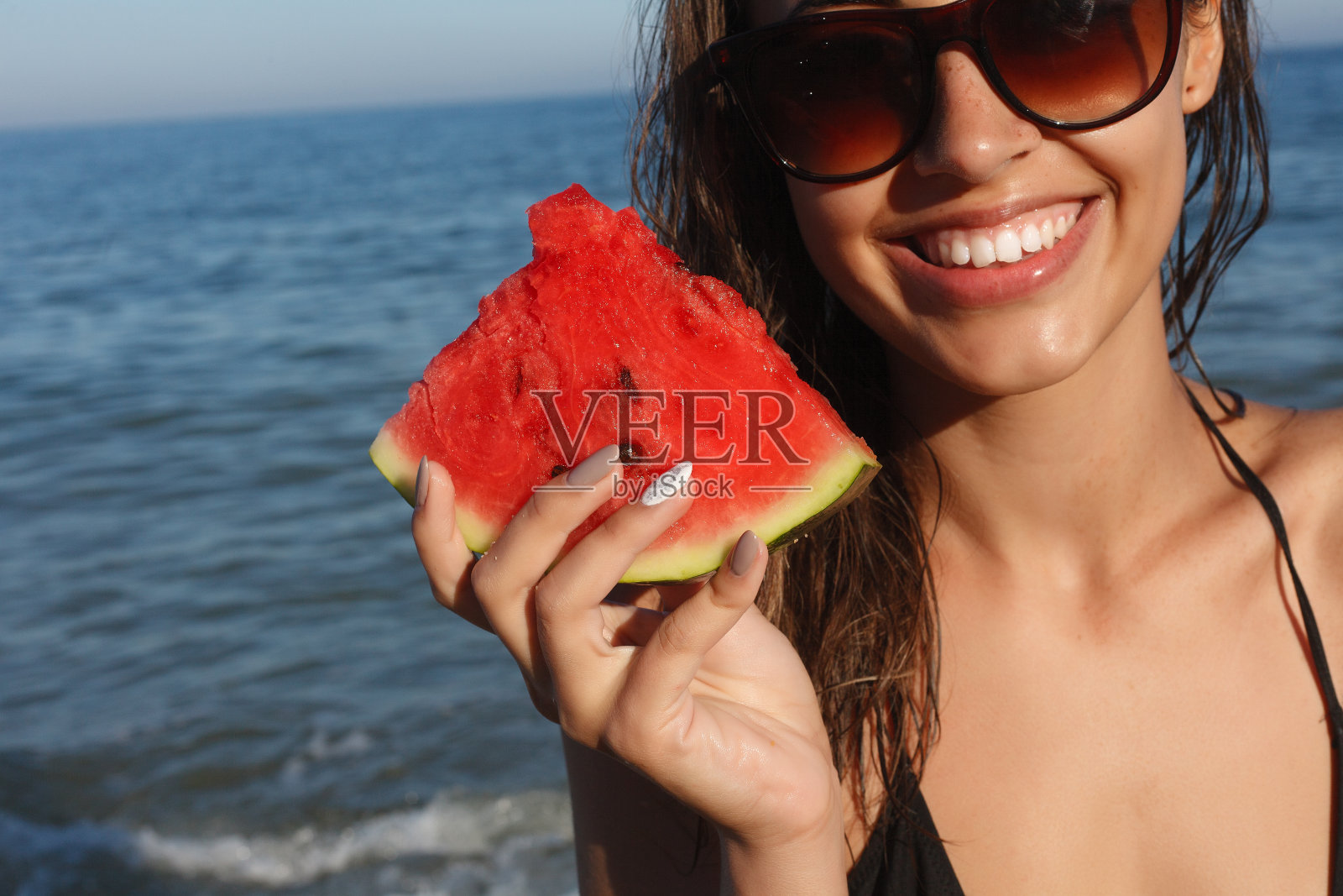 暑假——年轻女孩在沙滩上吃新鲜的西瓜照片摄影图片