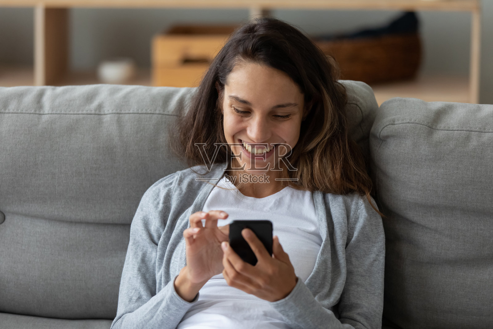 正面微笑的女人拿着电话，坐在舒适的沙发上照片摄影图片