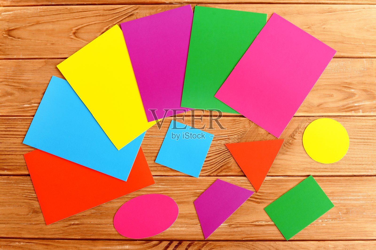 纸板切成三角形、正方形、椭圆形、梯形、长方形、圆形。儿童教育的概念。木桌上放着一张张彩色纸板。彩色纸板几何形状照片摄影图片