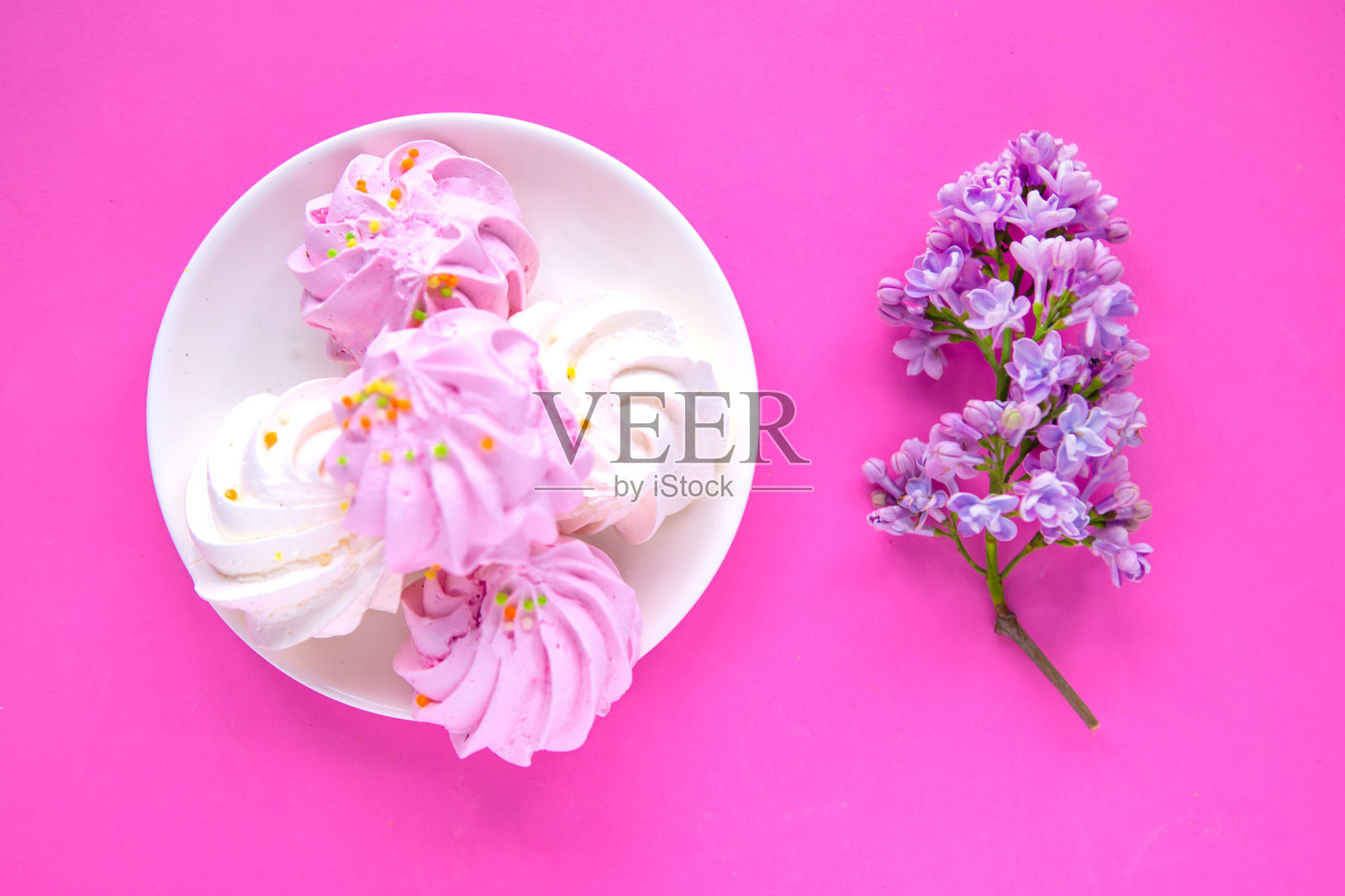 鲜嫩美味的蛋白酥皮和盛开的丁香枝在明亮的粉红色背景下，俯视图，平铺照片摄影图片