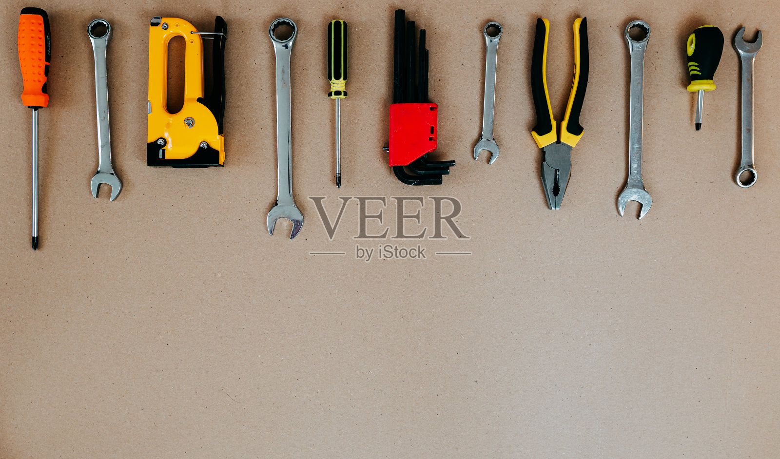 工具在牛皮纸上俯视图。钳子、开口扳手、螺丝刀和钉书钉枪平放在复印处。照片摄影图片