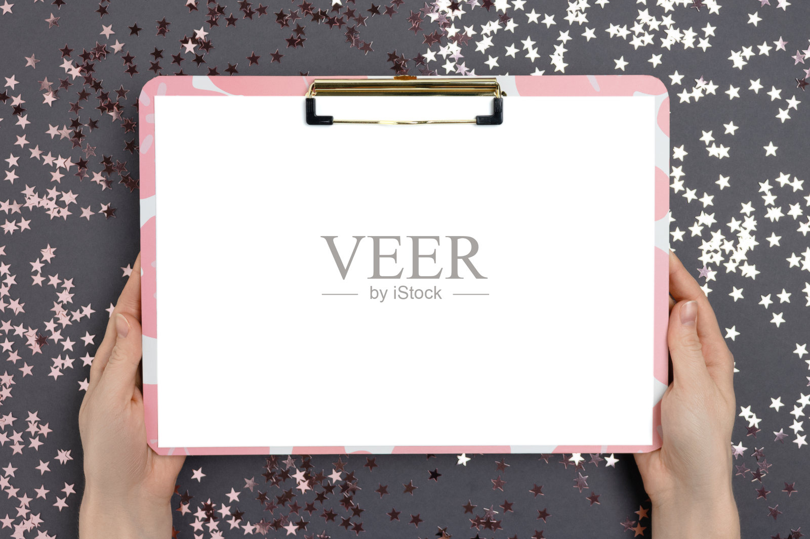 女性手里拿着空白纸的剪贴板。粉色闪亮的星星纹理。照片摄影图片