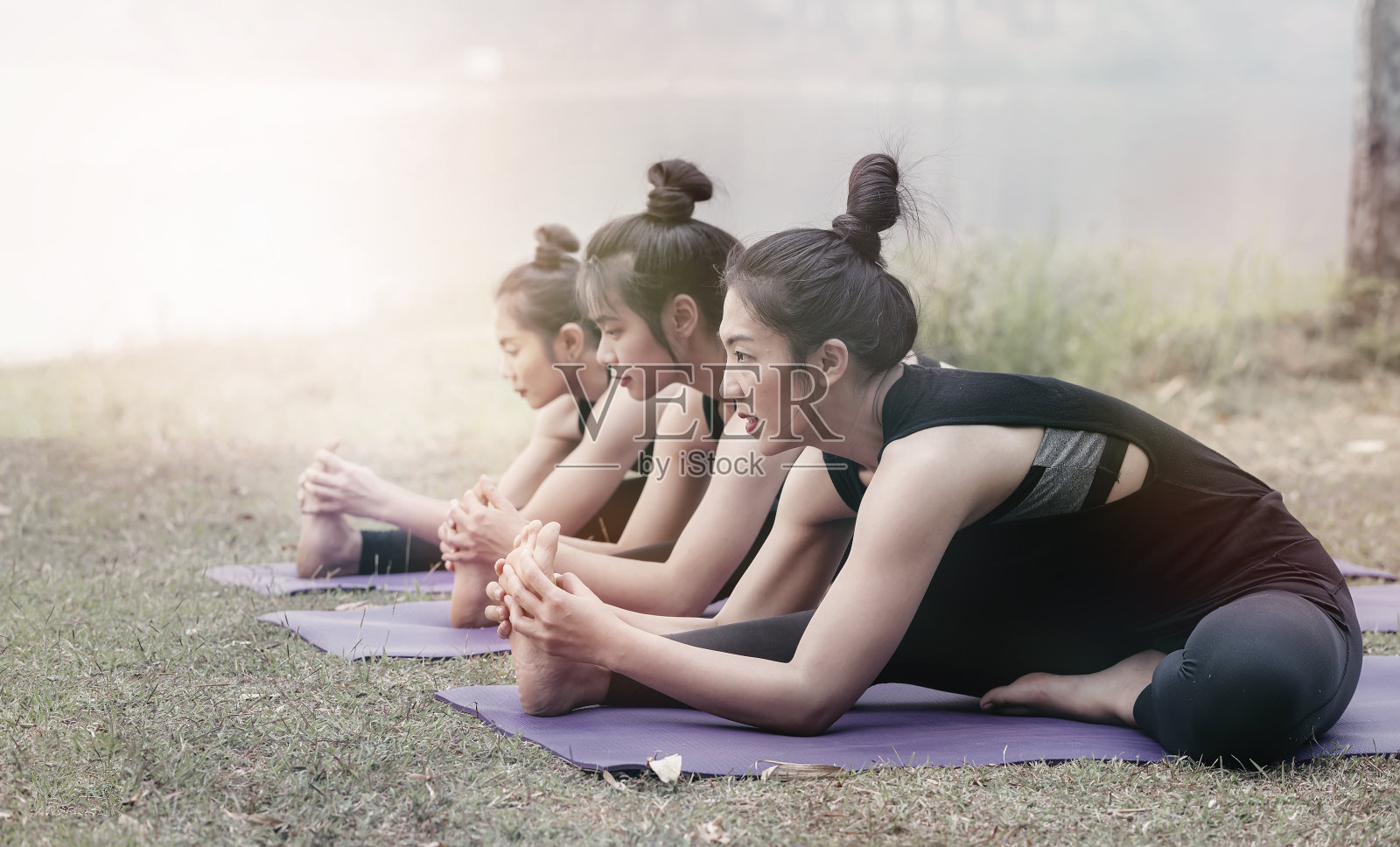 一群年轻的亚洲女性穿着黑色运动服在公园里练习瑜伽。照片摄影图片