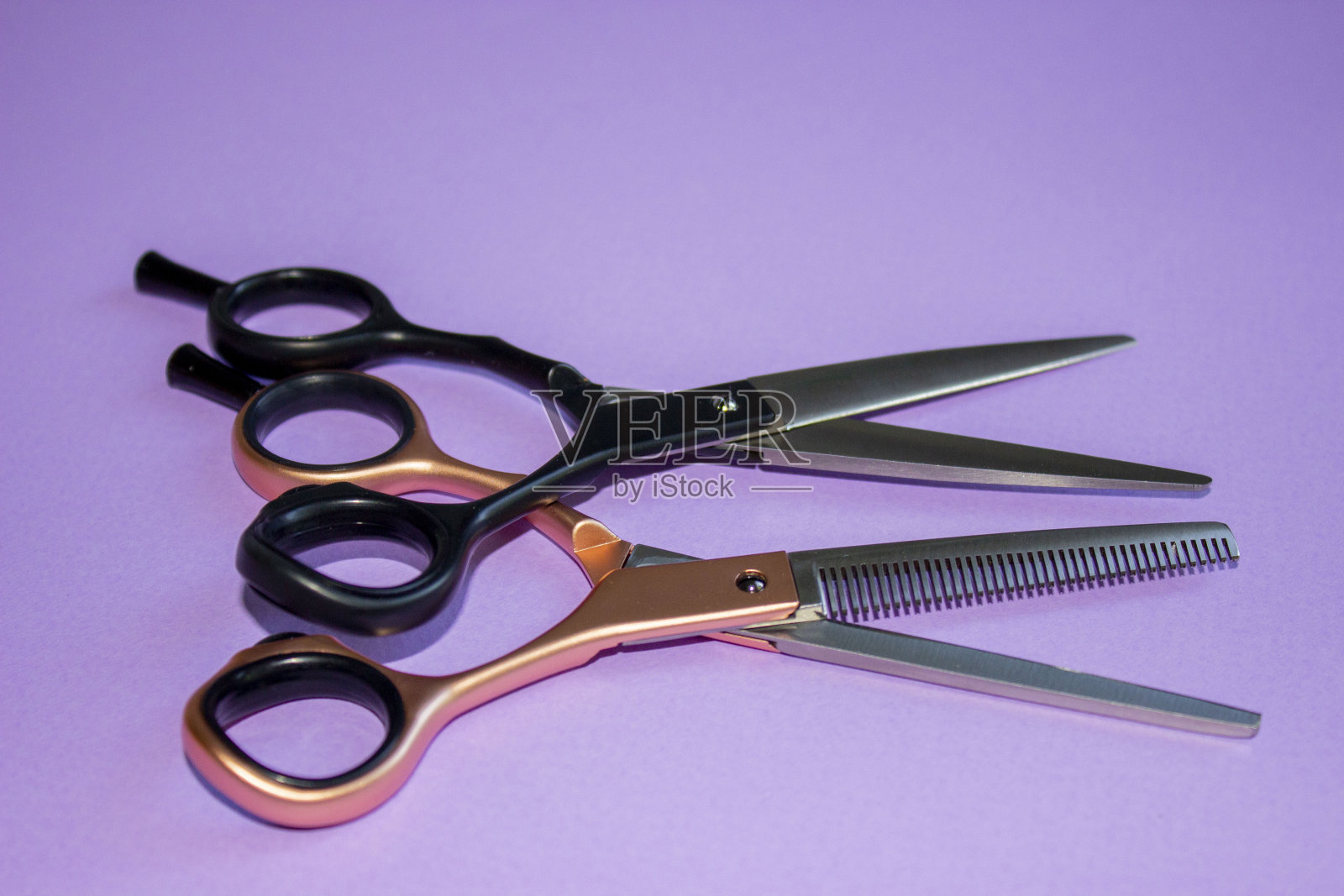 美发剪刀。夫妇。对于理发来说，黑色和玫瑰金色的锉子，在开阔的地方，彼此叠在一起。固体紫色背景。基地,横幅,明信片。照片摄影图片