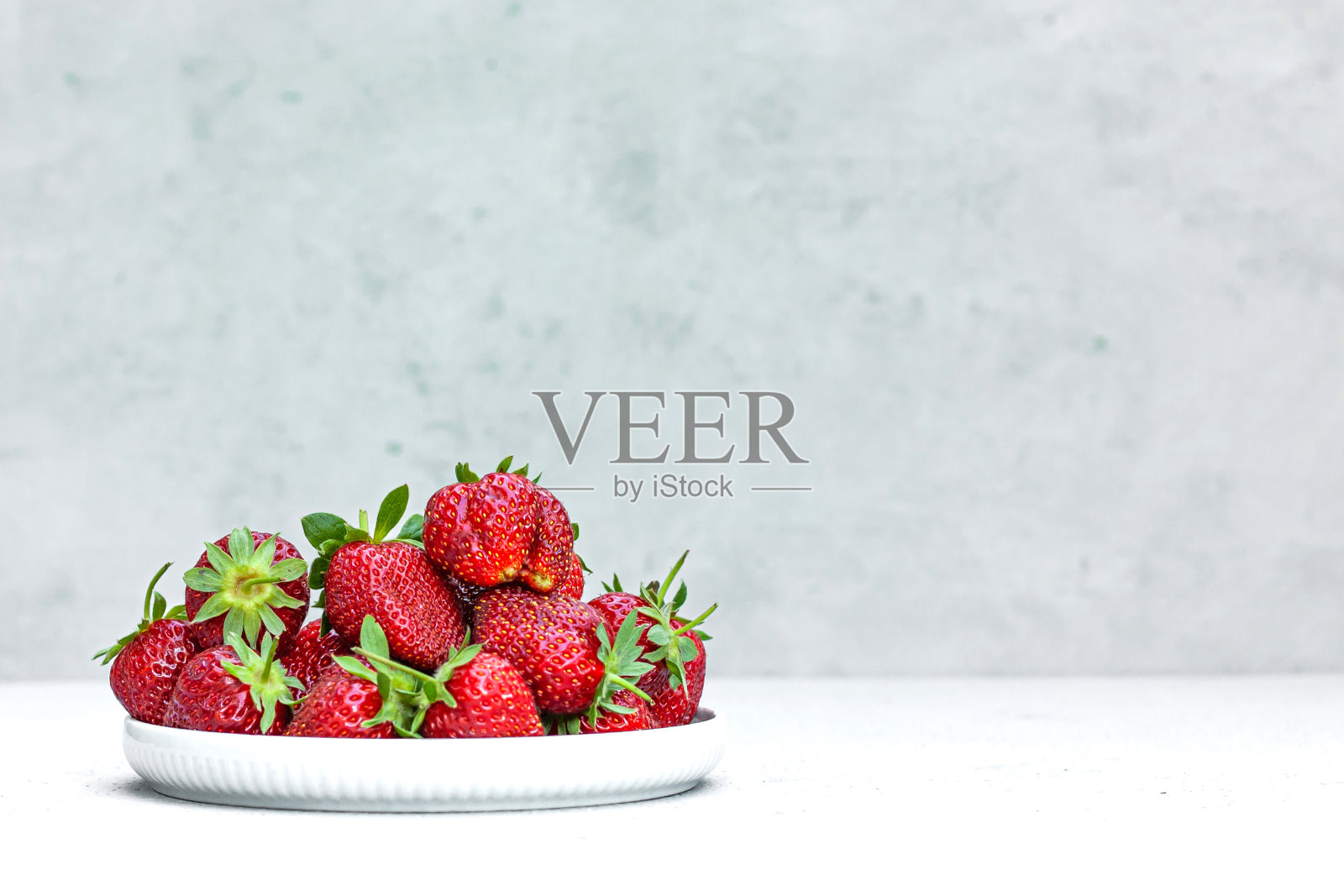 新鲜成熟的有机草莓放在一个白色的碗里。多汁的红色美味的浆果在灰色的背景。空间的文本。健康饮食的概念。照片摄影图片