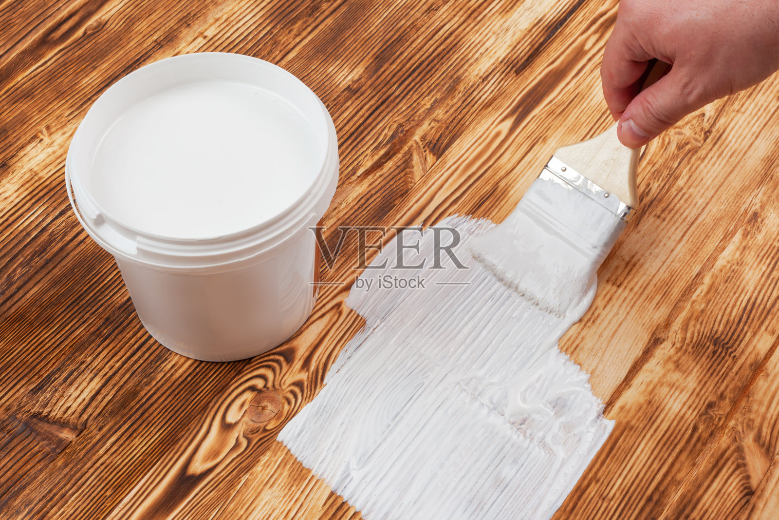 一罐白油漆立在一个烧焦的刷过的表面上，男性用刷子手油漆照片摄影图片