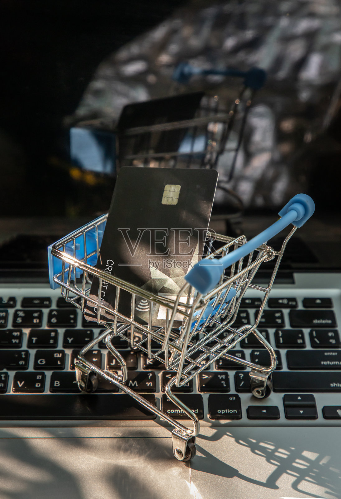 迷你超市手推车里的一张信用卡放在笔记本电脑键盘上。照片摄影图片