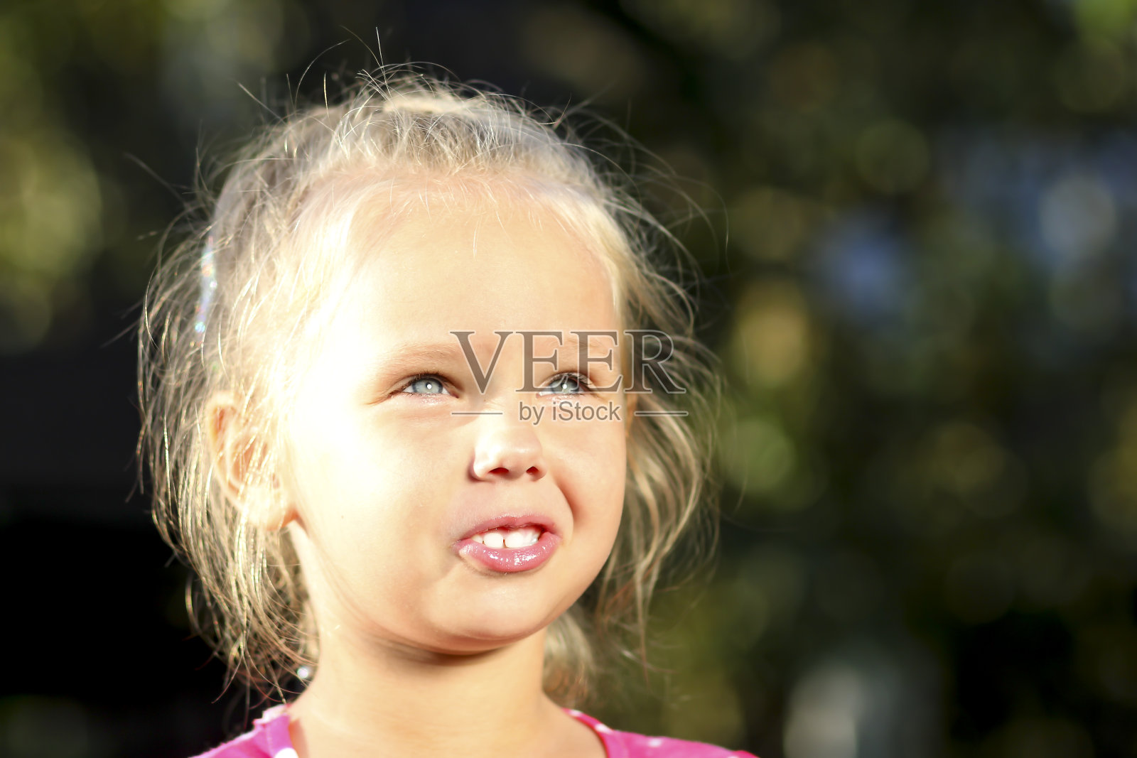 一个快乐的小女孩眯着眼睛看着明亮的太阳。关闭了。金发碧眼的女孩。儿童保护日概念照片摄影图片