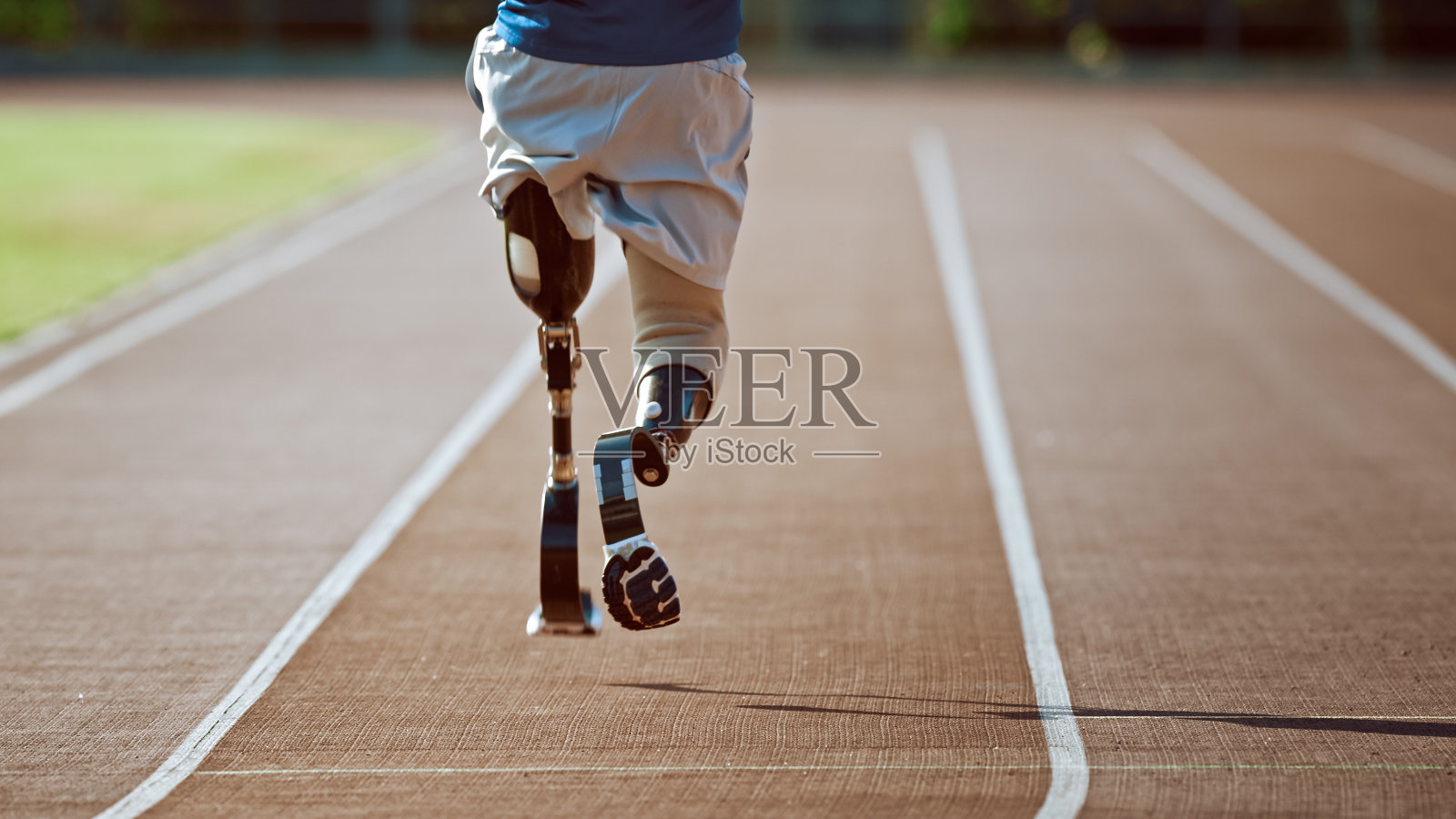 运动残疾人健美儿戴着义肢跑步刀片在阳光明媚的下午在户外体育场训练。截肢跑步者在体育场跑道上慢跑。激励运动镜头。的腿。照片摄影图片