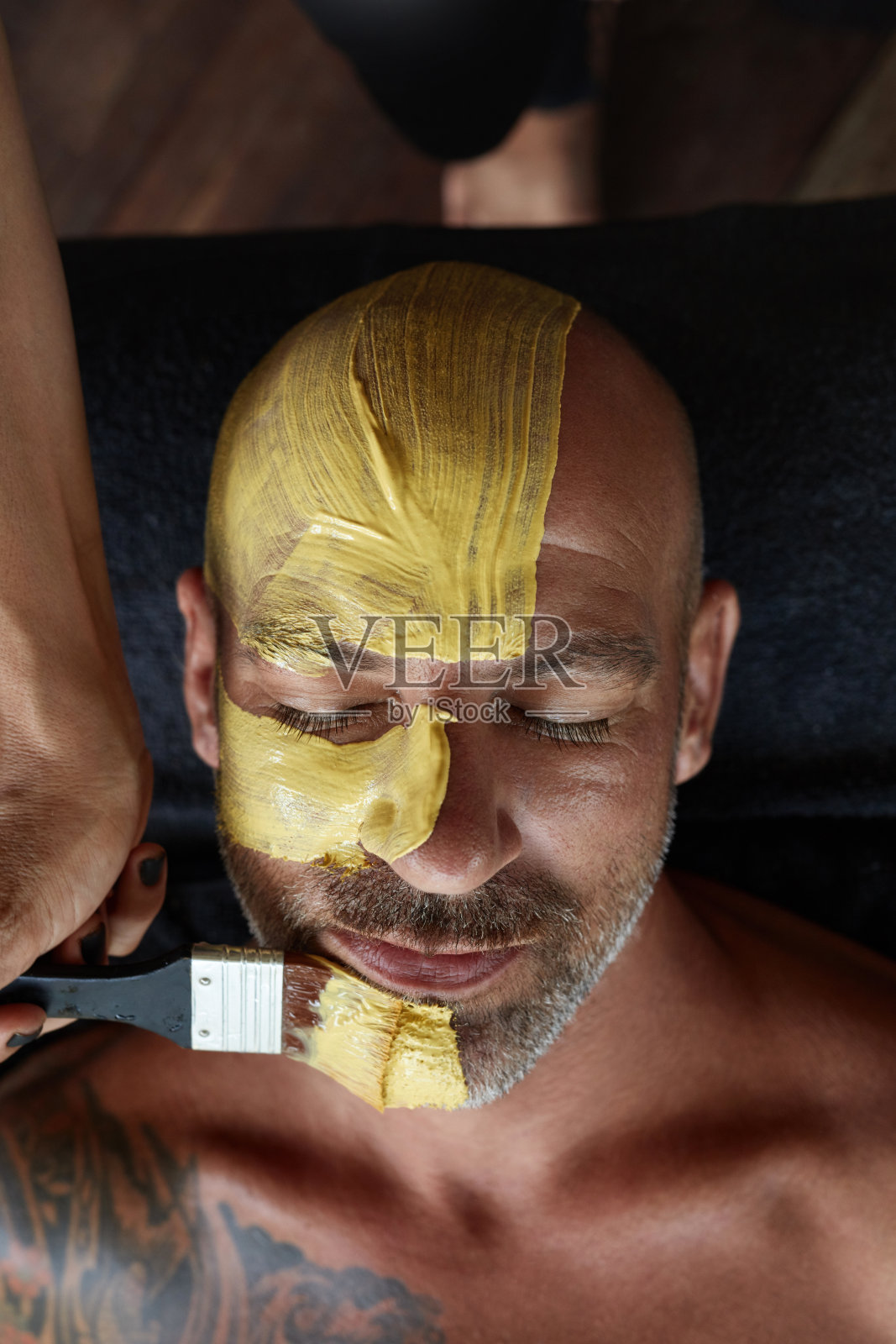Spa面罩。美容护理皮肤。美容师在男人脸上涂黄泥。自然美容手术的放松模型。照片摄影图片